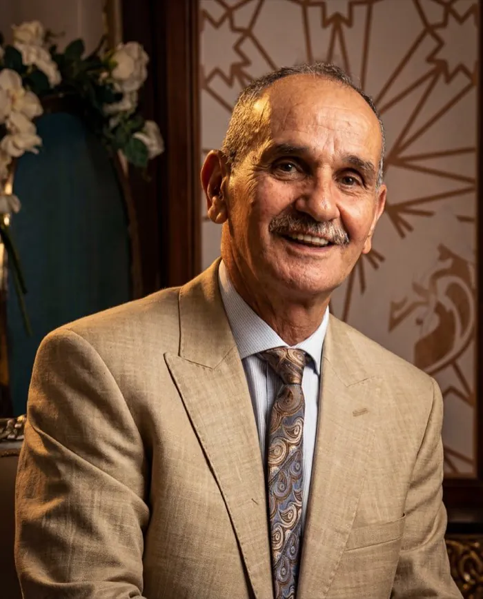 Jamal smiling, in a beige suit and patterned tie.